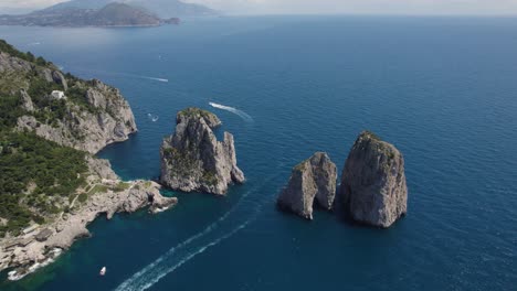 Boat-traffic-along-dramatic-Capri-coastline,-Faraglioni-aerial-view