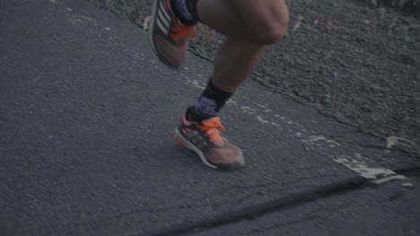 Close-up-shot-of-professional-runners-feet-and-legs-running-on-paved-road-in-slow-motion-at-dusk-shot-in-HD