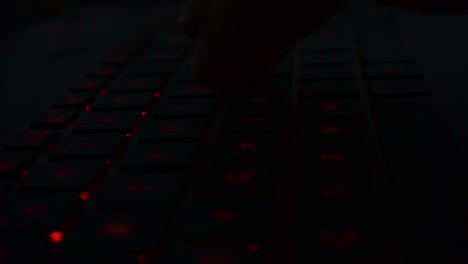 Close-up-shot-of-hand-typing-on-red-lighting-keyboard-of-laptop-in-dark-room