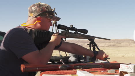 Hunter-at-outdoor-desert-range,-adjusting-R25-rifle-bipod,-slider-shot