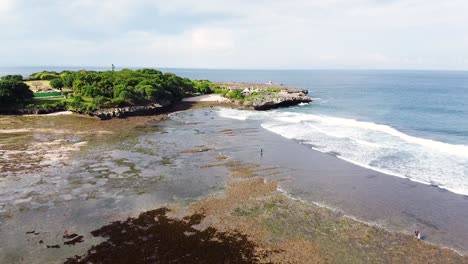 Drone-shot-of-beach-cliffs,-reefs-and-religious-statues-in-Bali