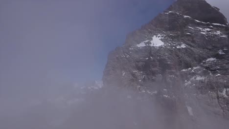 Peak-of-Mount-Cervino,-Mont-Cervin,-The-Matterhorn-seen-from-drone-emerging-from-clouds-to-reveal-steep-rugged-terrain-and-the-Carrel-Hut