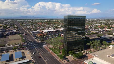 4K-Drone-ascending-beside-a-high-rise-office-building-with-reflective-windows-with-mountains-in-the-background-and-Cumulonimbus-clouds-in-the-sky-and-light-traffic-turning-onto-a-street