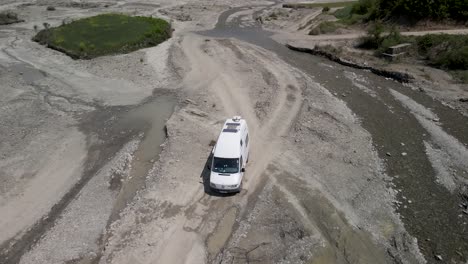 Camper-driving-on-unpaved-gravel-road-near-small-river