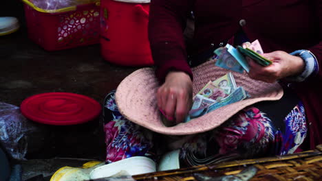 Vietnamese-street-scene,-woman-counting-money-inside-big-hat