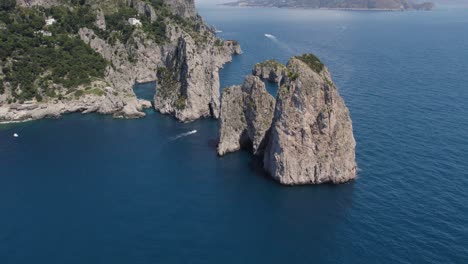 Sheer-cliff-faces-of-dramatic-Faraglioni-sea-stacks,-Capri-coastline-aerial