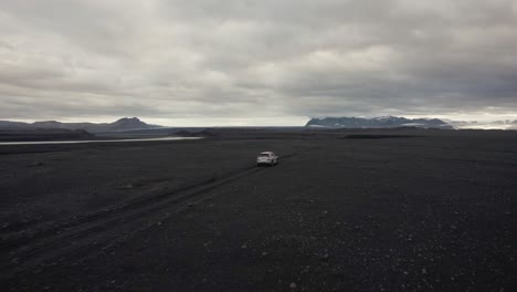 Drone-following-a-silver-car-in-a-lava-field-flying-upwards-with-the-camera-tilting-down-in-Iceland-4k