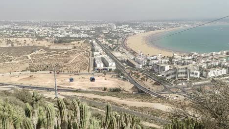 Cable-car-of-the-aerial-tramway-connecting-Oufella-peak-and-Agadir-city-in-Morocco,-overlooking-a-panoramic-view-of-the-beach-6