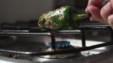 Hand-Turning-Green-Bell-Pepper-Roasting-Over-Stove-Fire-In-The-Kitchen