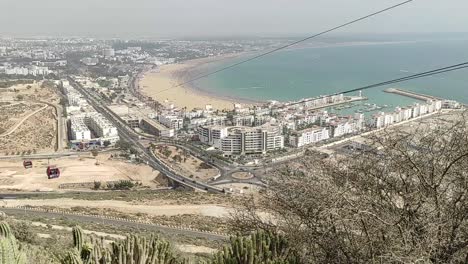 Cable-car-of-the-aerial-tramway-connecting-Oufella-peak-and-Agadir-city-in-Morocco,-overlooking-a-panoramic-view-of-the-beach-21