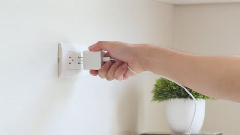 Person-plugging-a-phone-charger-into-the-wall-plug
