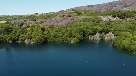 Aerial-panning-view-Dorothea-slate-mining-quarry-woodland-in-Snowdonia-valley-with-gorgeous-shimmering-blue-lake