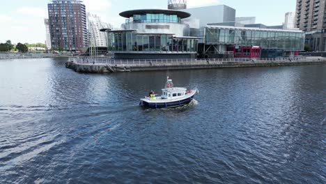 Aerial-drone-flight-over-Salford-Quays-at-Media-City-and-Manchester-Ship-Canal-following-a-small-fishing-Boat-as-it-travels-along-the-water