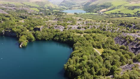Aerial-view-Dorothea-slate-mining-quarry-woodland-in-Snowdonia-valley-mountains-with-gorgeous-shimmering-blue-lakes