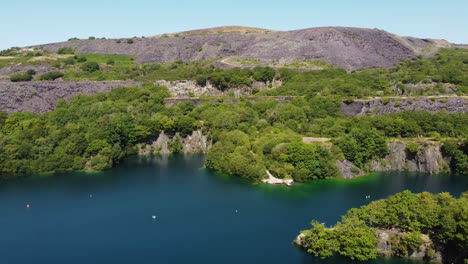 Aerial-view-Dorothea-flooded-slate-mining-quarry-woodland-in-Snowdonia-valley-with-gorgeous-shimmering-turquoise-lake