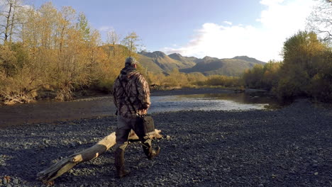 A-nature-and-wildlife-photographer-walks-across-a-salmon-river-in-preparation-for-a-fall-photoshoot-in-the-wilderness-of-Kodiak-Island-Alaska