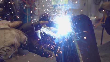 Gloved-hands-holding-welding-torch-with-bright-sparks-flying,-steel-craftsman