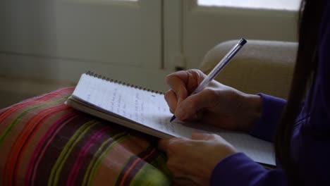 Mujer-Sentada-En-Un-Sofá-Escribiendo-Notas-Durante-Su-Clase-En-El-Cuaderno-En-Su-Regazo