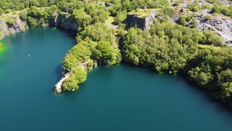 Aerial-view-Dorothea-flooded-mining-quarry-woodland-in-Snowdonia-valley-with-gorgeous-clear-blue-lake