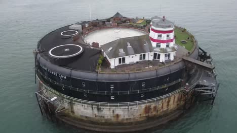 Aerial-drone-flight-around-the-Solent-Fort-structure-in-the-English-Channel-in-the-Isle-of-Wight-showing-the-red-and-white-Lighthouse-and-gardens