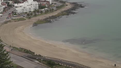 Aerial-time-lapse-shot-of-couple-and-dog-walking-along-sandy-beach-during-cloudy-day-in-Uruguay