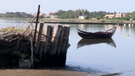 Un-Barco-Amarrado-En-El-Río,-Con-Estacas-De-Madera-Sosteniendo-Una-De-Las-Orillas