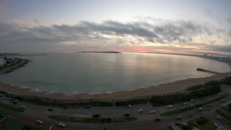 Aerial-timelapse-of-beautiful-sunset-at-horizon-in-Punta-del-Este-Beach,Uruguay---Traffic-on-road-in-the-evening