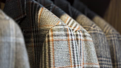 Grey-patterned-tweed-jackets-hanging-in-wooden-wardrobe,-close-up