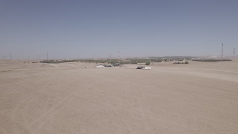 Bedouin-tents-in-an-arid-and-remote-area,-on-a-dry-sand-field-off-the-grid,-near-large-power-lines-and-an-animal-feed-factory-parallax-shot-1