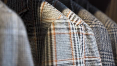 Patterned-tailored-tweed-jackets-hanging-in-wooden-wardrobe,-close-up