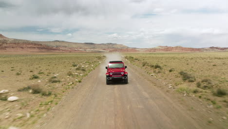 Red-Jeep-Wrangler-Driving-Through-Dusty-Dirt-Road-Of-Desert-In-Utah