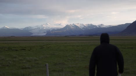 Man-walking-away-in-shot-of-Iceland-prairie-and-mountains