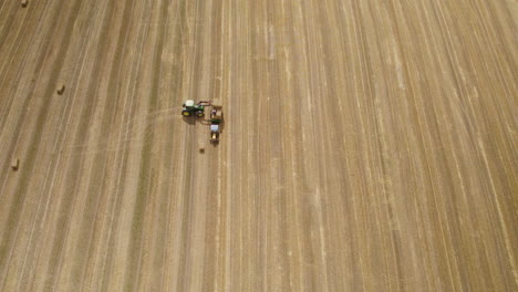 Aerial-top-down-of-tractor-loading-hay-bales-on-transporter-after-harvesting-on-wheat-field-in-summer