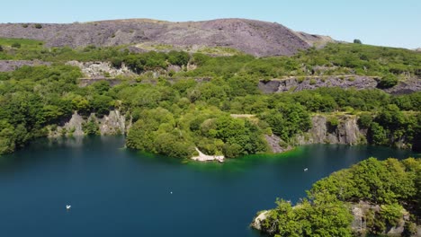 Aerial-view-Dorothea-flooded-slate-mine-quarry-woodland-in-Snowdonia-valley-with-gorgeous-shimmering-blue-lake