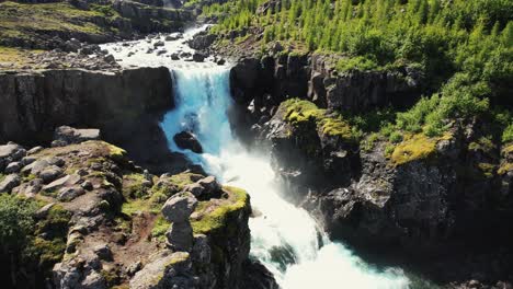 Tiro-De-Drone-Girando-Hacia-Arriba-Sobre-Una-Gran-Cascada-Con-Un-Arco-Iris-Y-Montañas-En-El-Fondo-En-Islandia-4k