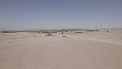 Bedouin-tents-in-an-arid-and-remote-area,-on-a-dry-sand-field-off-the-grid,-near-large-power-lines