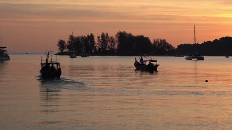 Traditional-fishing-boat-cruising-forward,-fisherman-out-to-the-sea-to-catch-fish-at-sunset-with-beautiful-orange-sky-and-calm-water-reflection,-tropical-summer-vibe-at-Langkawi-Island,-Malaysia