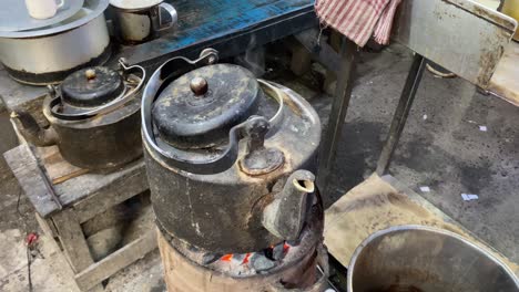 In-a-street-in-Kolkata,-a-kettle-of-water-is-boiling-over-a-clay-burner-or-chullah-a-type-of-stove
