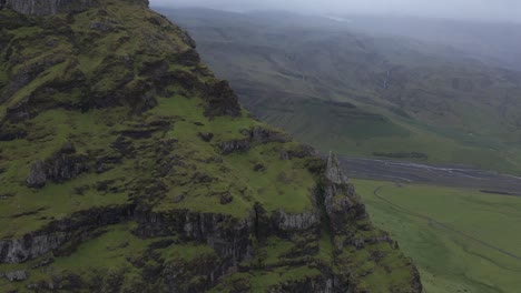Grand-green-moss-rock-cliff-with-rainy-weather-in-Iceland,-aerial