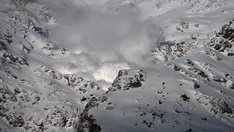 A-foggy-avalanche-is-going-down-a-Rocky-mountain-in-the-Swiss-alps,-science-phenomenon