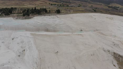 Aerial-of-white-travertine-terraces-thermal-pools-in-Pamukkale-Turkey-Hierapolis-in-background-drone