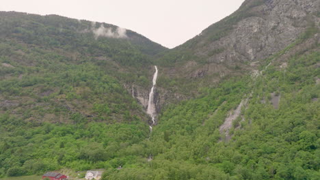 Waterfall-cascades-into-Laerdal-valley-covered-in-farm-land,-Norway