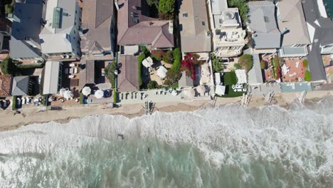 Pacific-ocean-waves-almost-hitting-luxury-homes-in-Malibu,-aerial-top-down-view