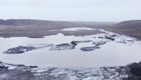 Calved-icebergs-in-glacial-lagoon-at-Kvíarjökull-glacier-on-cloudy-day,-aerial
