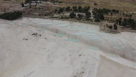 Drone-of-white-thermal-pool-terraces-in-Pamukkale-Turkey-with-historic-hierapolis-background
