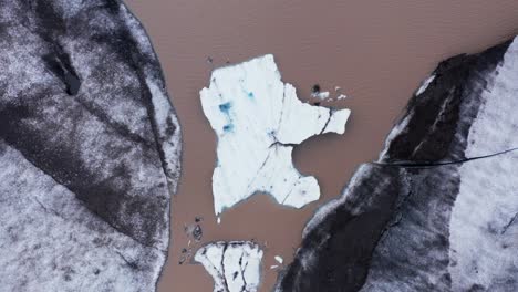 Frozen-iceberg-in-brown-glacial-lagoon,-melting-by-climate-change,-top-down