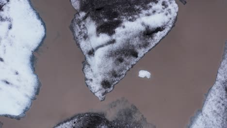 Frozen-icebergs-with-black-ash-on-surface-floating-in-brown-glacial-lagoon-water