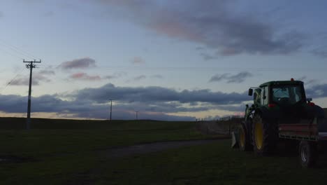 Farm-sunset-with-parked-tractor-on-grass,-clouds-on-horizon,-telephone-lines