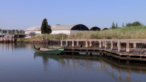 Angelsteg-Mit-Zwei-Booten-Und-Holzsteg-In-Der-Mitte-Des-Flusses,-Lagerhäuser-Im-Hintergrund-Auf-Der-Anderen-Uferseite