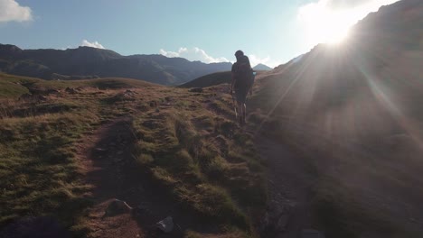 Back-view-of-Young-hiker-witg-backpack-and-trekking-pole-walking-towards-the-sun-in-Spanish-Pyrenees-during-sunset